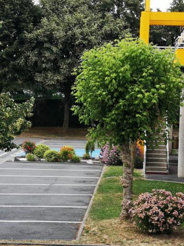 a tree in front of a parking lot with flowers at Premiere Classe Lille Sud - Seclin in Seclin