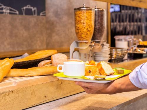 a person holding a plate with a cup of coffee and bread at ibis budget Paris Porte d'Italie Est in Le Kremlin-Bicêtre