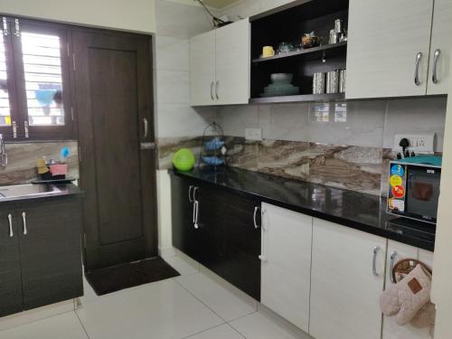 a kitchen with white cabinets and a black counter top at Swag Apartment in Mysore
