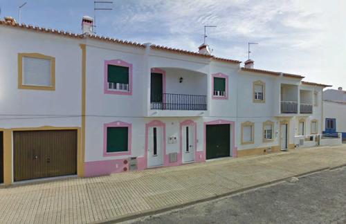 a large white building with pink doors on a street at Casa Cor-de-Rosa in Vila Nova de Milfontes