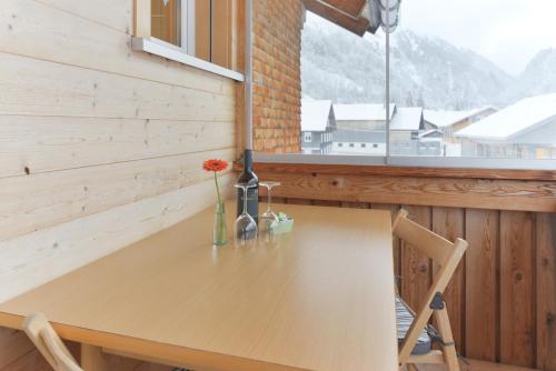 a wooden table with a vase of flowers and a window at Pension Haus Romy in Schoppernau