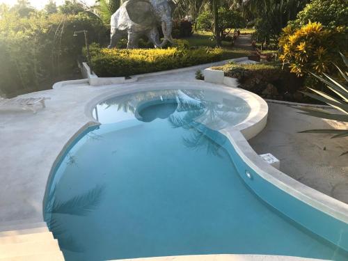 a blue swimming pool with a dinosaur statue in the background at Fortamu Twiga-House in Watamu