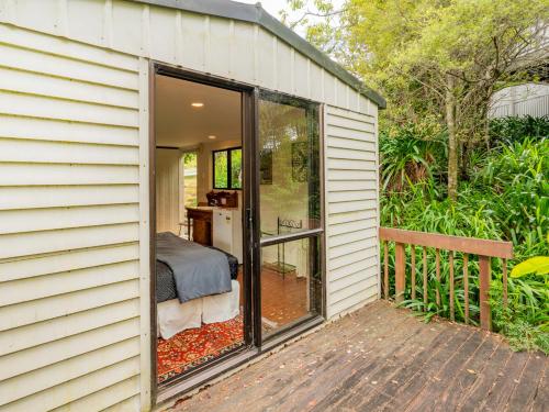 a small house with a bedroom and sliding glass doors at At Cathedral Cove - Hahei Holiday Home in Hahei