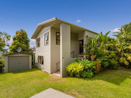 a white house with a garage in a yard at At Cathedral Cove - Hahei Holiday Home in Hahei