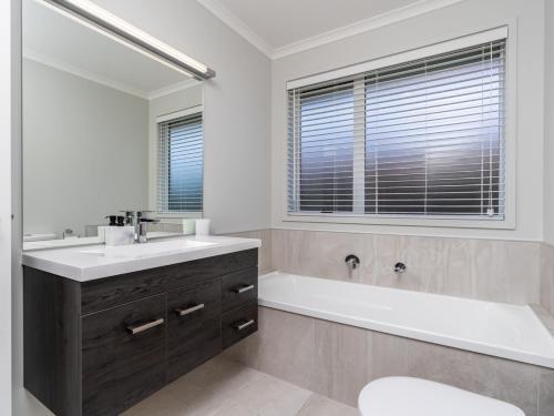 La salle de bains est pourvue d'un lavabo, d'une baignoire et d'un miroir. dans l'établissement First Choice in Mangawhai - Mangawhai Holiday Home, à Mangawhai