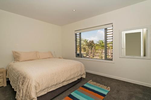 a white bedroom with a bed and a window at Matarangi Marvel - Matarangi Holiday Home in Matarangi