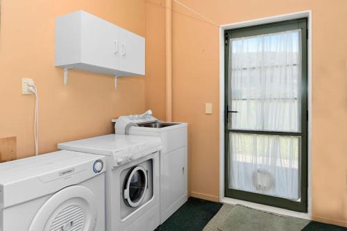 a laundry room with a washing machine and a window at Kiwi Kuta with direct beach access -Matarangi Home in Matarangi