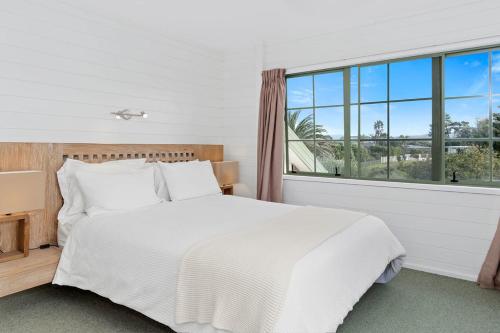 a bedroom with a white bed and a large window at Kiwi Kuta with direct beach access -Matarangi Home in Matarangi