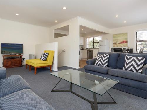 a living room with two blue couches and a glass table at Sand Castles - Mount Maunganui Holiday Home in Mount Maunganui