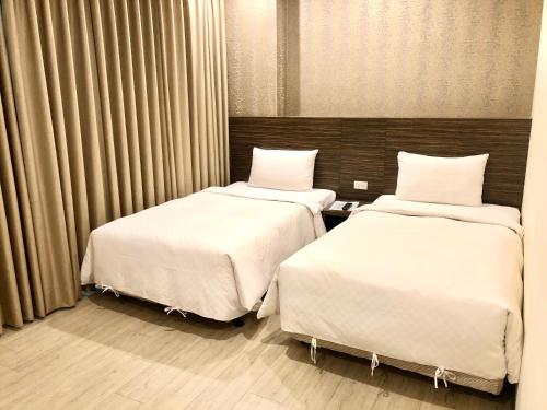 two beds in a hotel room with white sheets at Kousin Hotel in Kaohsiung