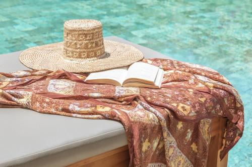 a hat and a book on a table next to a pool at The Pavilions Bali - CHSE Certified in Sanur