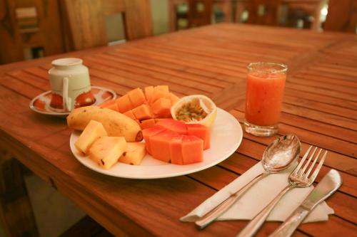 a plate of fruit on a wooden table with a drink at River Cottage in Wellawaya