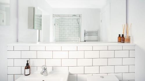 a white tiled bathroom with a sink and a mirror at Compton Lodge Luxury apartment-Free Parking in York