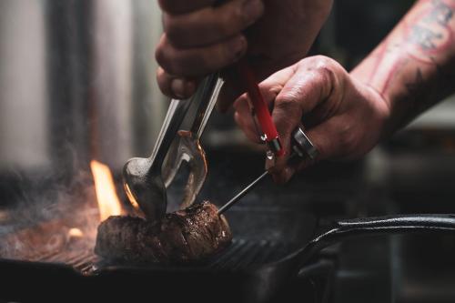 a person cooking meat on a grill with a pair of tongs at Skałka Zieleniec in Duszniki Zdrój