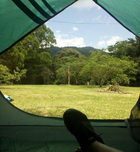 a person sitting in a tent looking out a window at a field at Camping do Delei in São Thomé das Letras