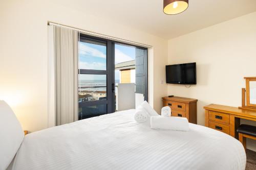 a bedroom with a white bed and a large window at West Beach - Holiday Apartments in Westward Ho
