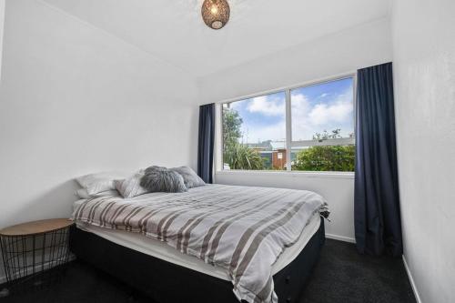 a bedroom with a bed and a large window at Archie's Beach Bach - Orewa Accommodation in Orewa