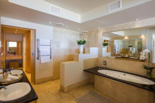 een badkamer met 2 wastafels, een bad en een spiegel bij Waves of Grace Seafront Villa in Herolds Bay