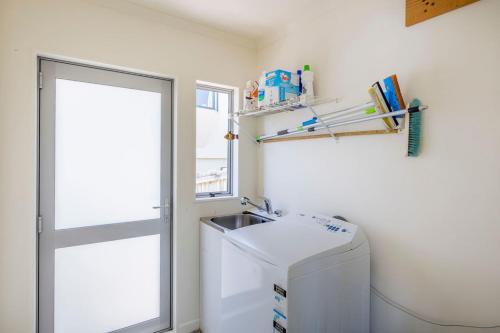 uma pequena cozinha com um lavatório e uma máquina de lavar roupa em Sun on Seaview - Paraparaumu Beach Holiday Home em Paraparaumu Beach
