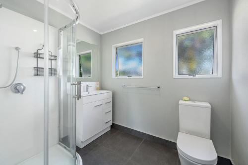 La salle de bains blanche est pourvue d'une douche et de toilettes. dans l'établissement Pohutukawa Breeze - Papamoa Beach Holiday Home, à Papamoa