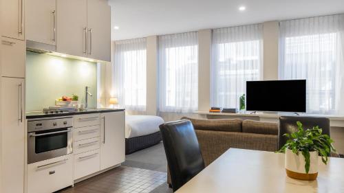 a kitchen and living room with a couch and a television at Oaks Melbourne on Collins Suites in Melbourne