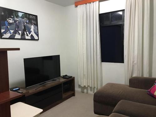 sala de estar con TV de pantalla plana y sofá en Quarto aconchegante nas Mercês en Curitiba