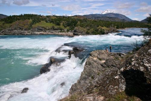 a person standing on the edge of a waterfall in a river at Lodge El Mirador De Guadal in Puerto Guadal