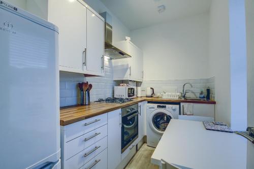 una cucina con armadi bianchi e una lavatrice/asciugatrice di Garden Gate Upper Apartment a Prestwick