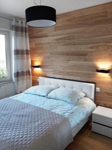 a bedroom with a white bed and a wooden wall at Apartament Szary Wilk in Świeradów-Zdrój