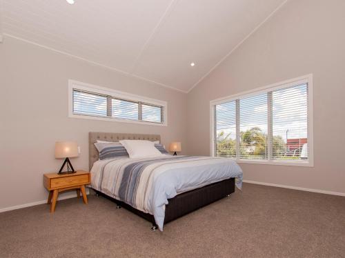 ein weißes Schlafzimmer mit einem Bett und zwei Fenstern in der Unterkunft Tattletails Rest - Whitianga Holiday House in Whitianga