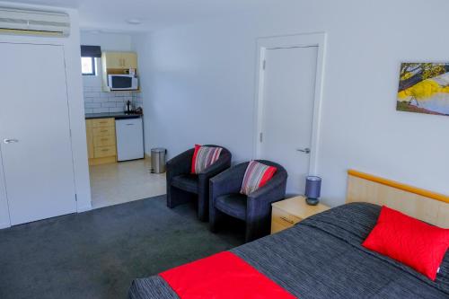 a bedroom with a bed and two chairs and a kitchen at ASURE Central Gold Motel Cromwell in Cromwell