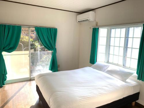 a bedroom with a bed with green curtains and a window at GANADAN Cottage in Kagoshima
