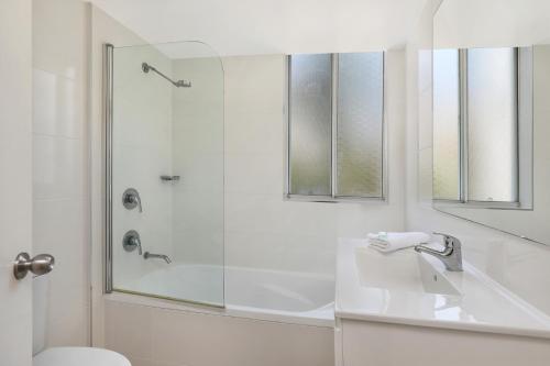 La salle de bains blanche est pourvue d'une douche et d'un lavabo. dans l'établissement The Bay Apartments Coolangatta, à Gold Coast