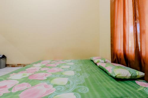 a bed with a green comforter with pink flowers at Penginapan Barokah in Kemadang
