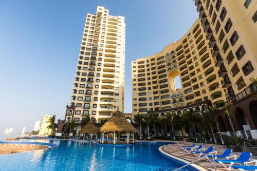 a hotel with a swimming pool in front of two tall buildings at Petit Luxe Las Gavias Penthouse in Mazatlán