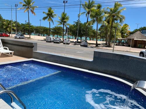 a large swimming pool next to a street with palm trees at Pajuçara Hotel Express in Maceió