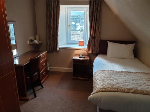 a bedroom with a bed and a desk and a window at Commercial Hotel in Alness
