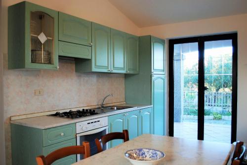 een keuken met groene kasten en een tafel met stoelen bij LE MAREE I LENTISCHI in San Teodoro