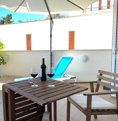a wooden table with wine glasses and an umbrella at Terrazza Montalbano in Punta Secca