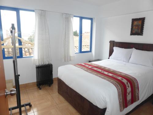 a bedroom with a bed with white sheets and windows at Apartment Samana House in Cusco