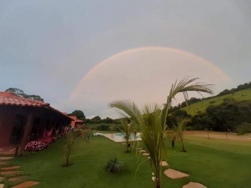 a rainbow over a yard with a house and a palm tree at Paraíso Capitólio Suítes Pousada in Capitólio