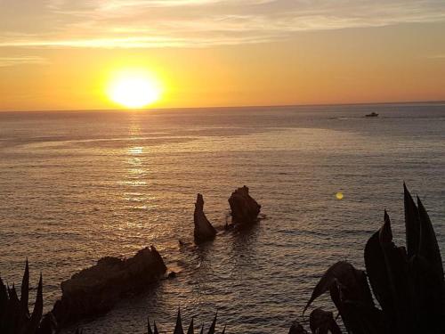 a sunset over the ocean with rocks in the water at Terra Sinus Holiday House in Terrasini