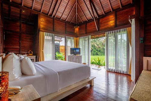 a bedroom with a large white bed in a room with windows at Kayangan Villa Ubud in Tegalalang