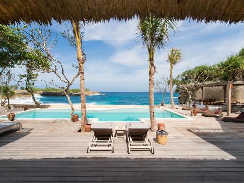a resort with a swimming pool and chairs and the ocean at Villa Voyage in Nusa Lembongan