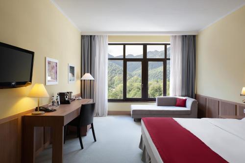 エストサドクにあるGolden Tulip Rosa Khutor Hotelのベッド、デスク、コンピュータが備わるホテルルームです。
