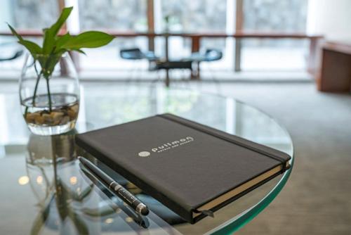 a book on a glass table with a pen and a vase at Pullman Doha West Bay in Doha