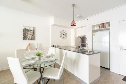 a white kitchen with a glass table and white chairs at S&P Apartments - Tank St in Brisbane