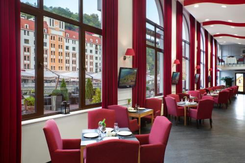 un restaurante con sillas rojas, mesas y ventanas en Tulip Inn Rosa Khutor Hotel, en Estosadok