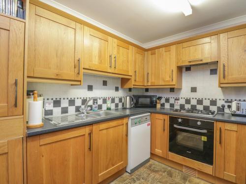 a kitchen with wooden cabinets and a white dishwasher at Kamba Cottage in Tannadice