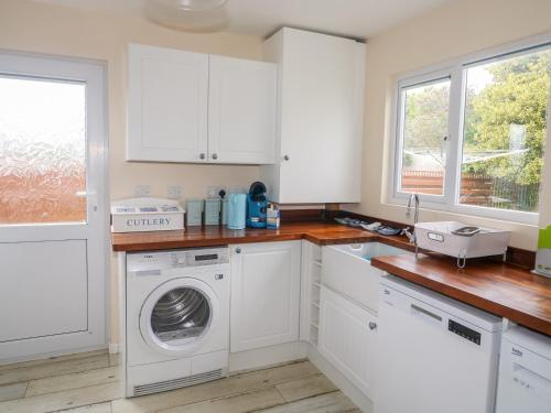 a kitchen with white cabinets and a washing machine at Merlin's Retreat in Tintagel